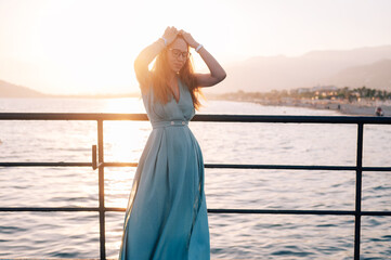 A woman in a flowing green dress poses on a pier by the sea at sunset, with a Turkey flag waving in the background.