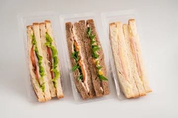 Three packaged sandwiches with white and whole wheat bread, filled with lettuce, tomatoes, turkey, cheese, ham and greens. Ideal for quick meals. © olinchuk