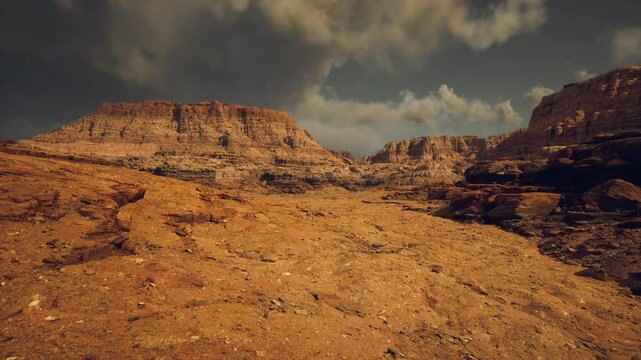 A vast rocky terrain stretches across the landscape, showcasing barren earth and towering cliffs beneath a moody, cloud laden sky. The rugged beauty evokes a sense of isolation and tranquility.