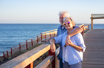 Handsome relaxed senior couple of retirees hugging face the sea enjoying vacation and free time at sunset. Horizon over water