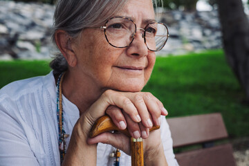 Portrait of a thoughtful elderly woman of 70 years old sitting on a bench in the park leaning on a...