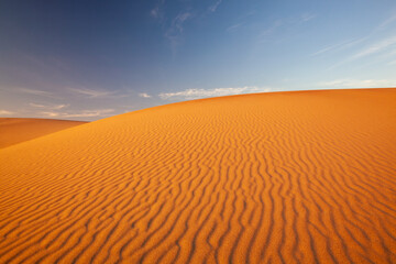 Sand dune at sunset, bright orange with wind ripples