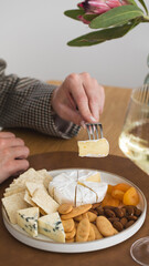 A glass of white wine in your hand against the background of a cheese plate with snacks and nuts
