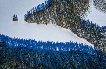 Aerial view on a lake covered with ice in Republiс of Karelia in winter in a sunny day. Shadows from the forest on the ice