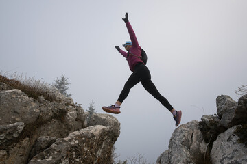 silhouette of a fitness woman trail runner jumping over a cliff and running to a rocky mountain top