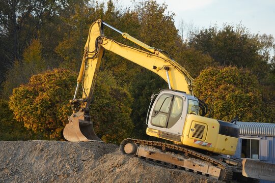 Excavator on a mound of earth illuminated by the evening sun