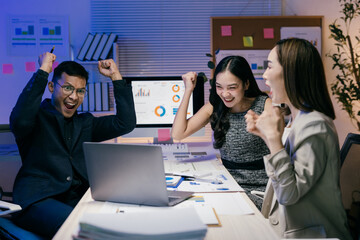 Group of asian businesspeople raising arms and cheering while working late in the office,...