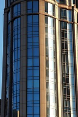 Fototapeta premium Modern urban skyscraper facade reflecting sunlight, showcasing architectural details, glass windows, metal accents, and contemporary design elements in a city environment.