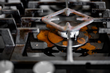 An extinguished gas burner with a coffee maker stand and spilled brewed coffee on the stove surface