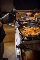 Chef frying cut vegetables in pan in restaurant kitchen.