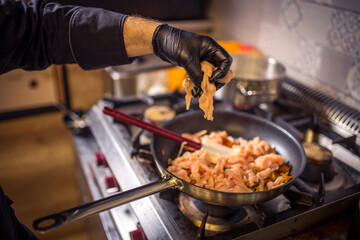 Chef frying cut vegetables and adds the chicken in pan in restaurant kitchen.