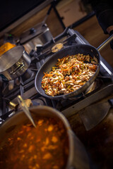 Chef frying cut vegetables and chicken in pan in restaurant kitchen.