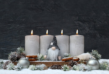 Vierter Advent: Dekoration mit vier grauen Adventskerzen einem Wichtel und Weihnachtsschmuck im...
