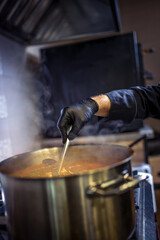 Chef in kitchen cooking in big pot green peas, beef, potatoes, onions with sauce.