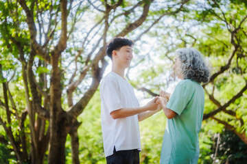 Young son and his mature mom asian people share loving hug in beautiful park, surrounded by nature. Their happiness radiates as they bond outdoors, celebrating family love and togetherness.