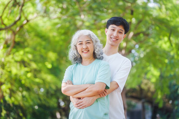 Fototapeta premium Young son and his mature mom asian people share loving hug in beautiful park, surrounded by nature. Their happiness radiates as they bond outdoors, celebrating family love and togetherness.