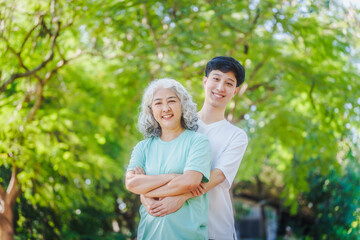 Obraz premium Young son and his mature mom asian people share loving hug in beautiful park, surrounded by nature. Their happiness radiates as they bond outdoors, celebrating family love and togetherness.