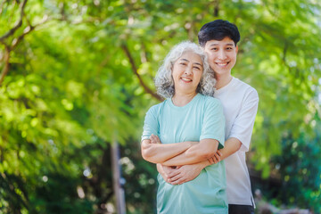 Young son and his mature mom asian people share loving hug in beautiful park, surrounded by nature. Their happiness radiates as they bond outdoors, celebrating family love and togetherness.