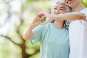 Fototapeta premium Young son and his mature mom asian people share loving hug in beautiful park, surrounded by nature. Their happiness radiates as they bond outdoors, celebrating family love and togetherness.