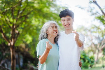 Fototapeta premium Young son and his mature mom asian people share loving hug in beautiful park, surrounded by nature. Their happiness radiates as they bond outdoors, celebrating family love and togetherness.