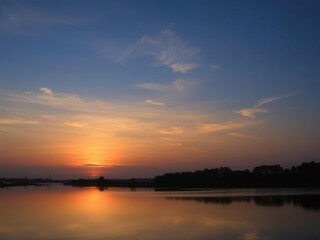 Vibrant sunrise over a calm lake with silhouetted trees in the foreground, reflection, silhouette, sky