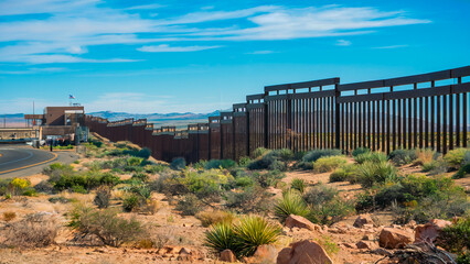 A scenic view of the US-Mexico border with a metal border fence stretching across a desert landscape under a clear blue sky. United States and Mexico.