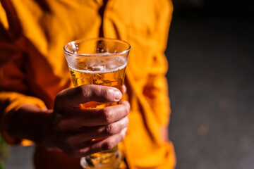 Asian man in yellow shirt enjoys a cold beer in a glass, alone during an evening party. The outdoor night sky sparkles as people celebrate with ice, creating vibrant celebration atmosphere.