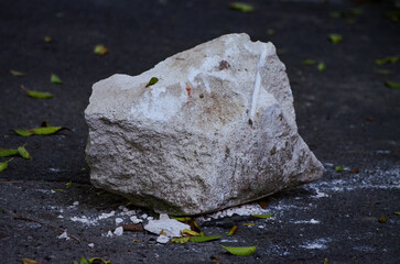 A large rock is sitting on the ground. The rock is covered in dirt and has a few leaves on it. The scene is quiet and peaceful, with the rock being the only object in the image.