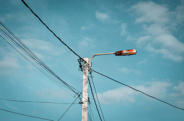 A street light is lit up in the daytime. The sky is blue and there are some clouds.