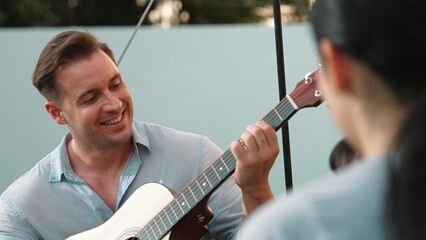 Family together camping. Mother and daughter listening father play guitar. Parent use outdoor...