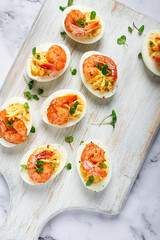 Boiled eggs stuffed with yolk and seasoned with mayonnaise, stuffed eggs with shrimp, on a white wooden chopping board, selective focus, close-up, without people,