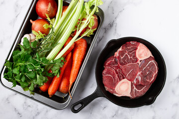 knuckle on the bone, raw meat for ossobuco, in a cast-iron pan, baking sheet with vegetables, top view, no people,