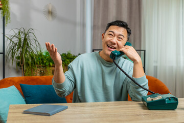 Middle-aged Asian man making wired telephone conversation with friends sitting call on couch at...
