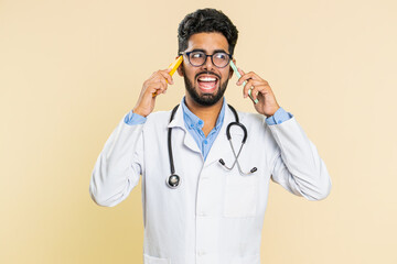 Irritated nervous stressed tired Indian doctor cardiologist man talking screaming on two mobile phones have conversation conflict quarrel. Arabian apothecary pharmacy guy isolated on beige background