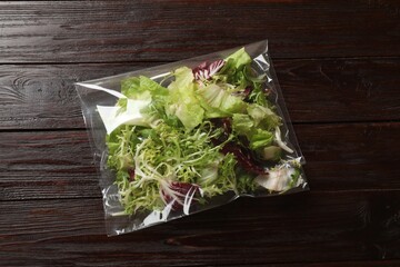 Pack of fresh salad mix on wooden table, top view