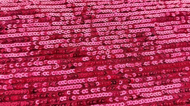 Close-up of vibrant pink-red sequin fabric with a densely packed, reflective texture and shimmering highlights