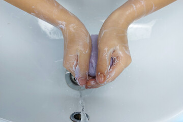 Children's hands with soap under running water in the sink. Clean hands after washing.