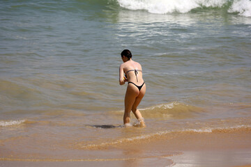 Young woman wearing thong bikini standing in sea waves. Beach vacation in hot weather