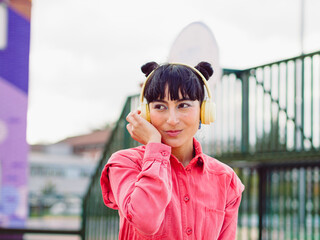 Latin hispanic woman whit  yellow headphones look away in the city while enjoy music whit buns...