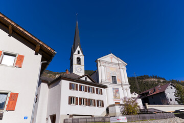 Fototapeta premium Looking up to church surrounded by houses at Swiss mountain village of Surava on a sunny autumn day. Photo taken November 15th, 2024, Surava, Switzerland.