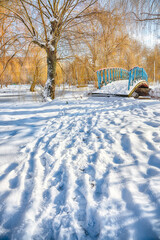 Fabulous landscape in city park with snowy trees and beautiful frozen river and footbridge