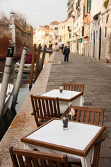 Cafe tables set out on the walkway next to a canal in Venice.
