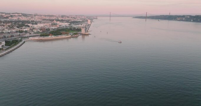 Aerial drone shot of the Tagus river, Atlantic Ocean and horizon at sunset in Lisbon, Portugal, Europe. Catamaran facing the sun. Forte do Bugio lighthouse visible. Shot in ProRes 422 HQ