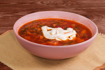 Red beet borscht seasoned with sour cream in pink bowl
