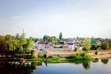 Fototapeta premium Small summer cottages among green trees on the bank of a clean river.