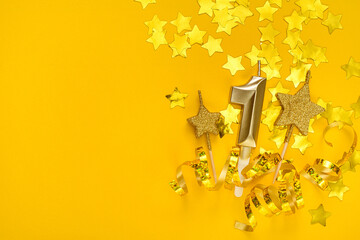 Gold candle in shape of number one on yellow background surrounded by stars confetti and streamers.