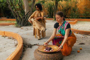 Indian musician in traditional clothes playing sitar festive season outdoor home. Woman in...
