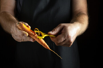 In a cozy kitchen illuminated by soft light, a cook peels vibrant carrots with focused hands. The orange and yellow vegetables glisten, showcasing their freshness and inviting colors