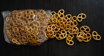 Salted pretzels on a black background poured out of a transparent pack. Top view. Pretzel