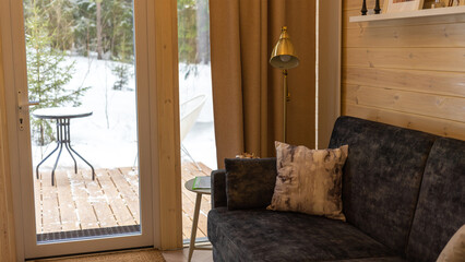 Interior of house with panoramic window in forest in winter. Lounge area with sofa and lamp in Scandinavian style Hygge. Cozy and comfortable interior made of natural materials